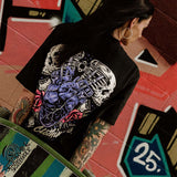 Tattooed female wearing an Omenz Full Throttle T-shirt and a skateboard in an urban graffiti street