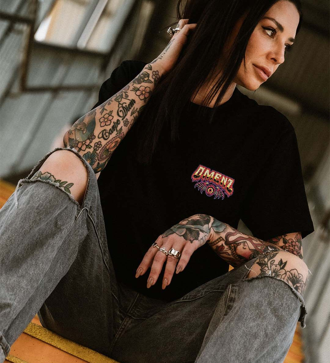 Tattooed female wearing denim shorts and an Omenz Killswitch T-shirt walking through an urban underpass