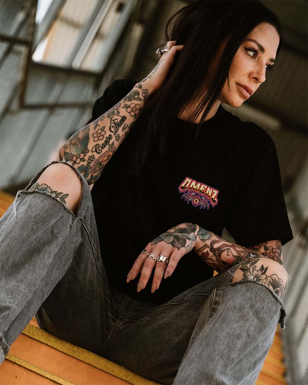 Tattooed female wearing denim shorts and an Omenz Killswitch T-shirt walking through an urban underpass