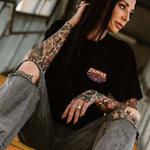 Tattooed female wearing denim shorts and an Omenz Killswitch T-shirt walking through an urban underpass